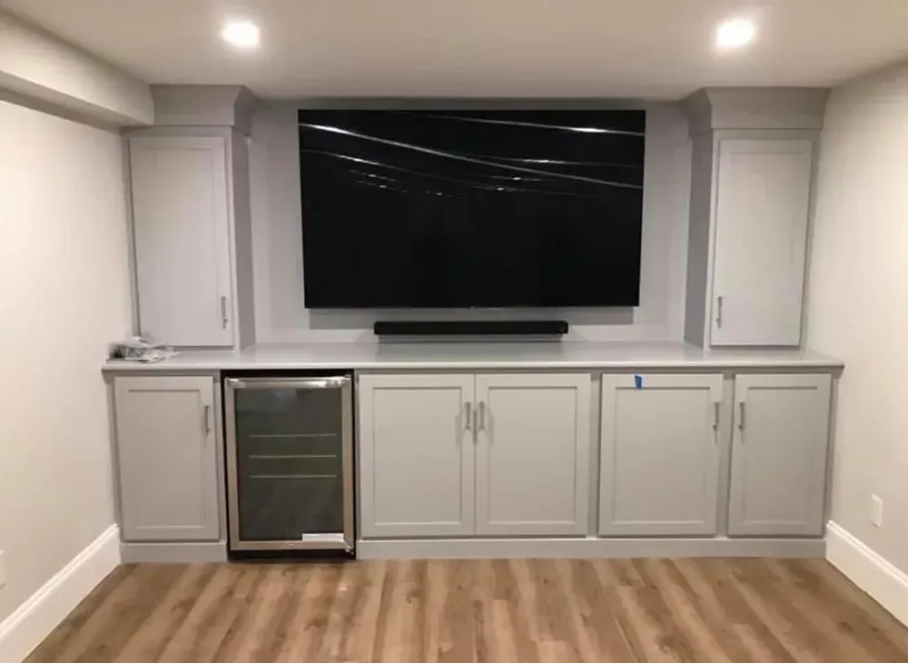 Built-in entertainment center with a large TV, soundbar, and cabinetry; a beverage cooler is on the left.