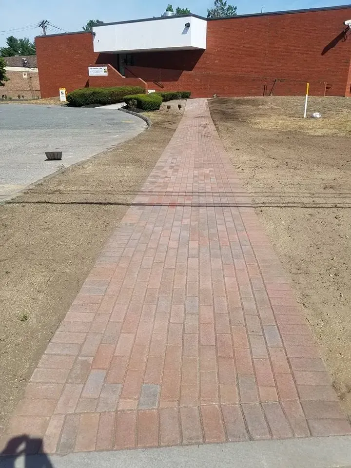 Brick walkway leading to a brick building. The walkway is surrounded by newly graded lawn