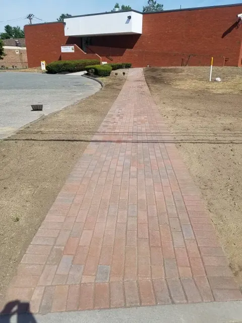 Brick walkway leading to a brick building. The walkway is surrounded by newly graded lawn