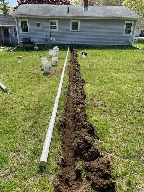 Trenched lawn with a long PVC pipe beside a house during yard work