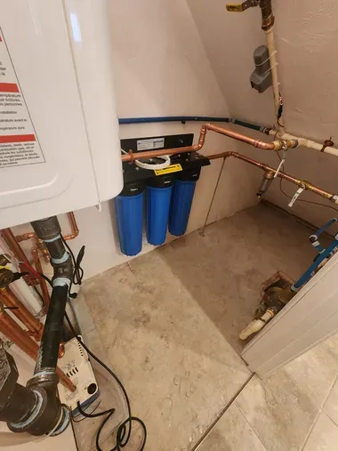 Utility room with water heater, copper pipes, and blue filters on a concrete floor