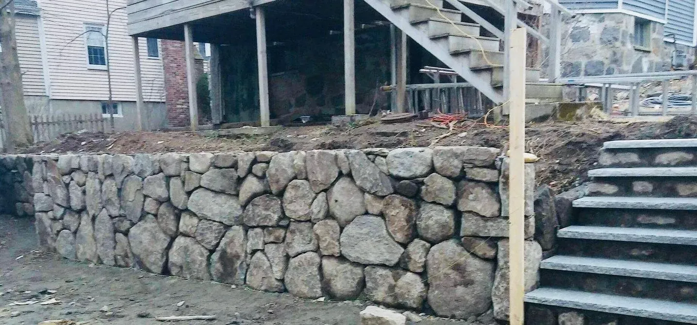 Stone retaining wall beside outdoor staircase and deck under a house