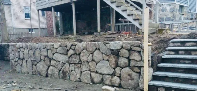 Stone retaining wall beside outdoor staircase and deck under a house