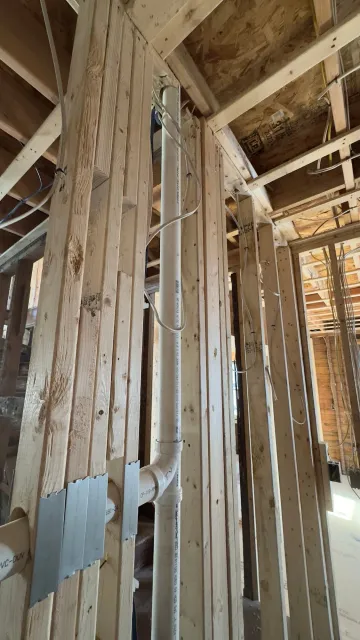 Interior view of a building under construction. White PVC pipe runs vertically through wooden beams.