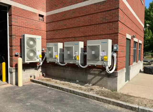 Outdoor HVAC units beside a red brick building on a concrete pad.