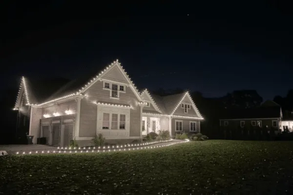 Home exterior illuminated with outdoor lighting and Christmas lighting. White lights outline the roofline and walkway, creating a festive ambiance against the night sky.
