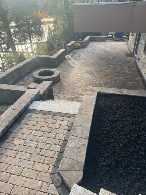 A stone patio with a fire pit, low retaining walls, and a landscaped garden bed, viewed from above.