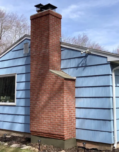Brick chimney attached to a blue house with a black cap on top