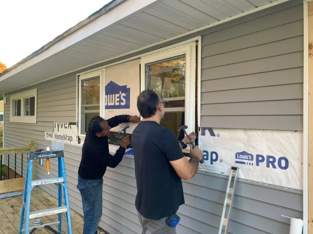 Two men are working on a window on the side of a house.