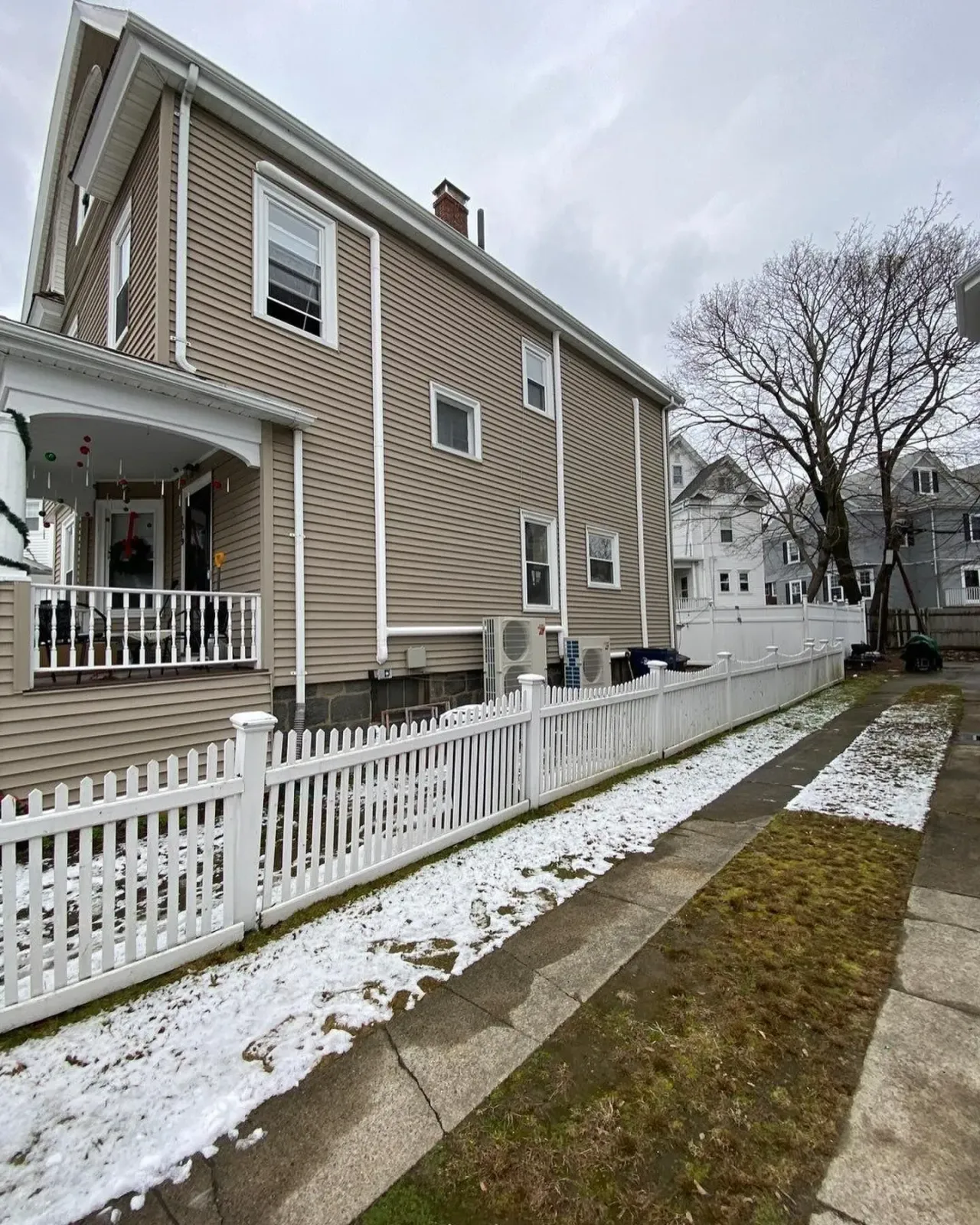 a house with a white picket fence and snow on the sidewalk in front of it