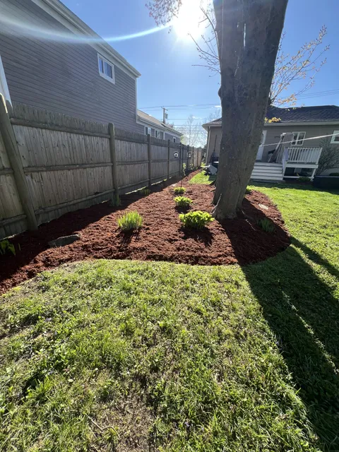 Fresh red mulch bed along a backyard fence line