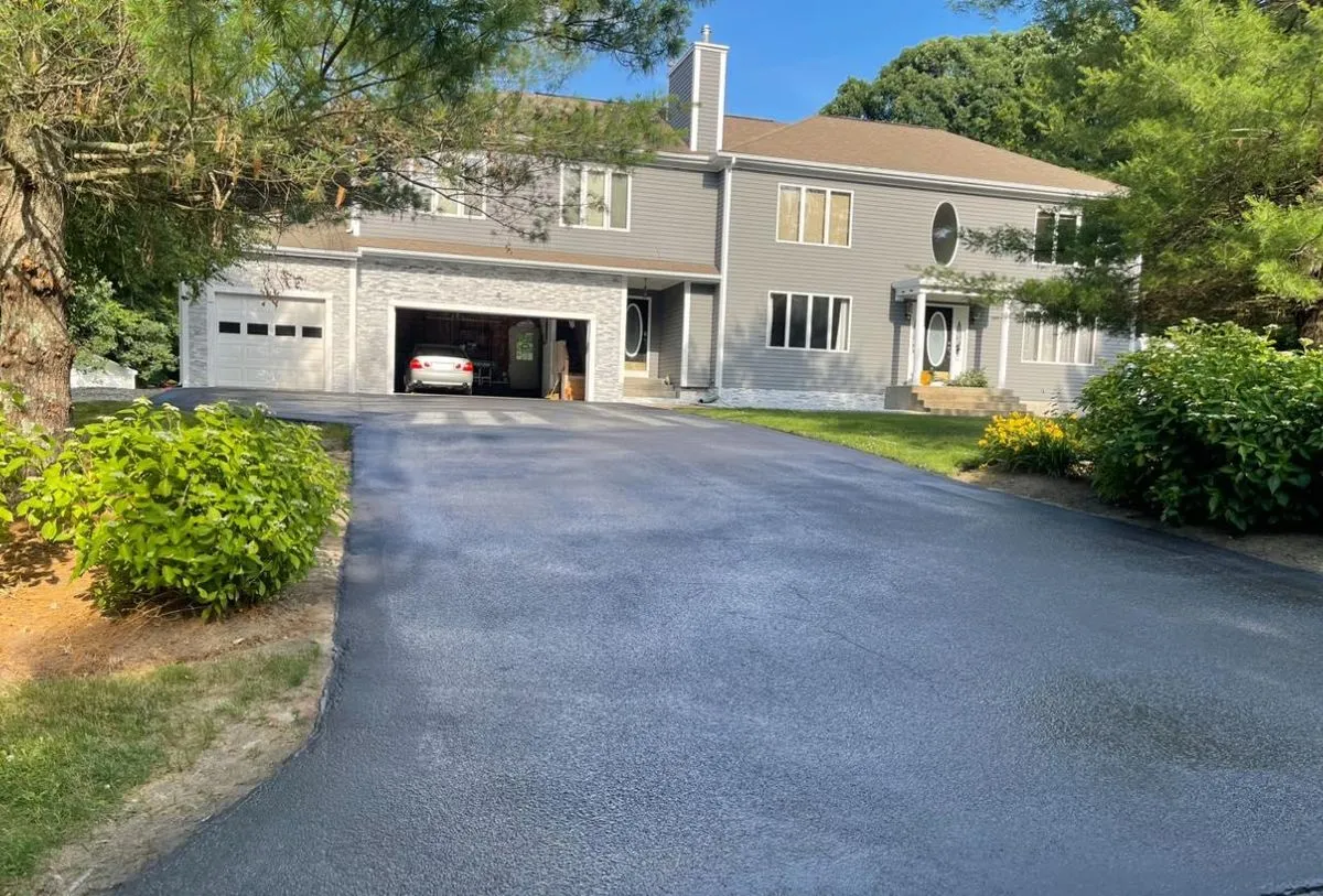 New asphalt driveway curving up to a large home with an open two car garage