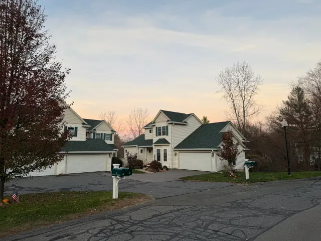 Suburban homes with garages and leafless trees at dusk, viewed from a driveway and street.