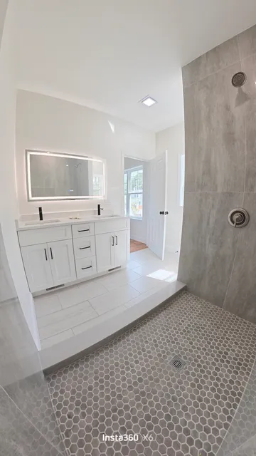 Completed bathroom remodel with a tiled walk-in shower, double vanity, and lighted mirror