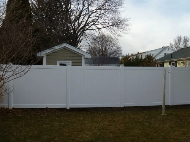 A white fence surrounds a backyard with a house in the background.