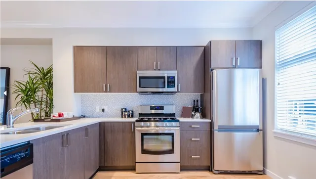 Modern kitchen with taupe wood-grain cabinets, white countertops, mosaic backsplash, and stainless appliances
