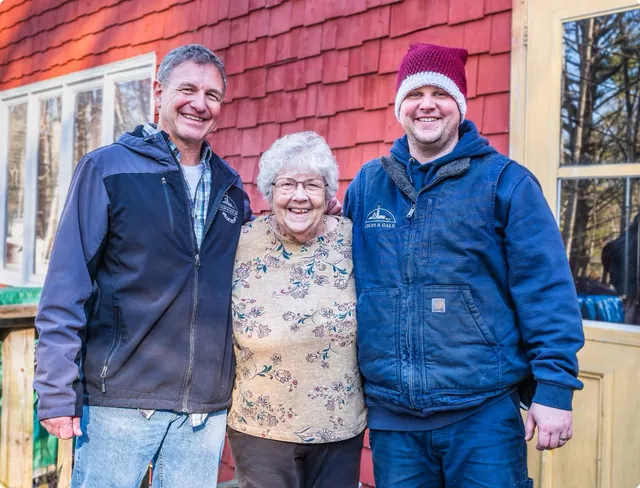 Colby & Gale team members Cappy and Nick posing with a satisfied customer outside their home in Midcoast Maine.