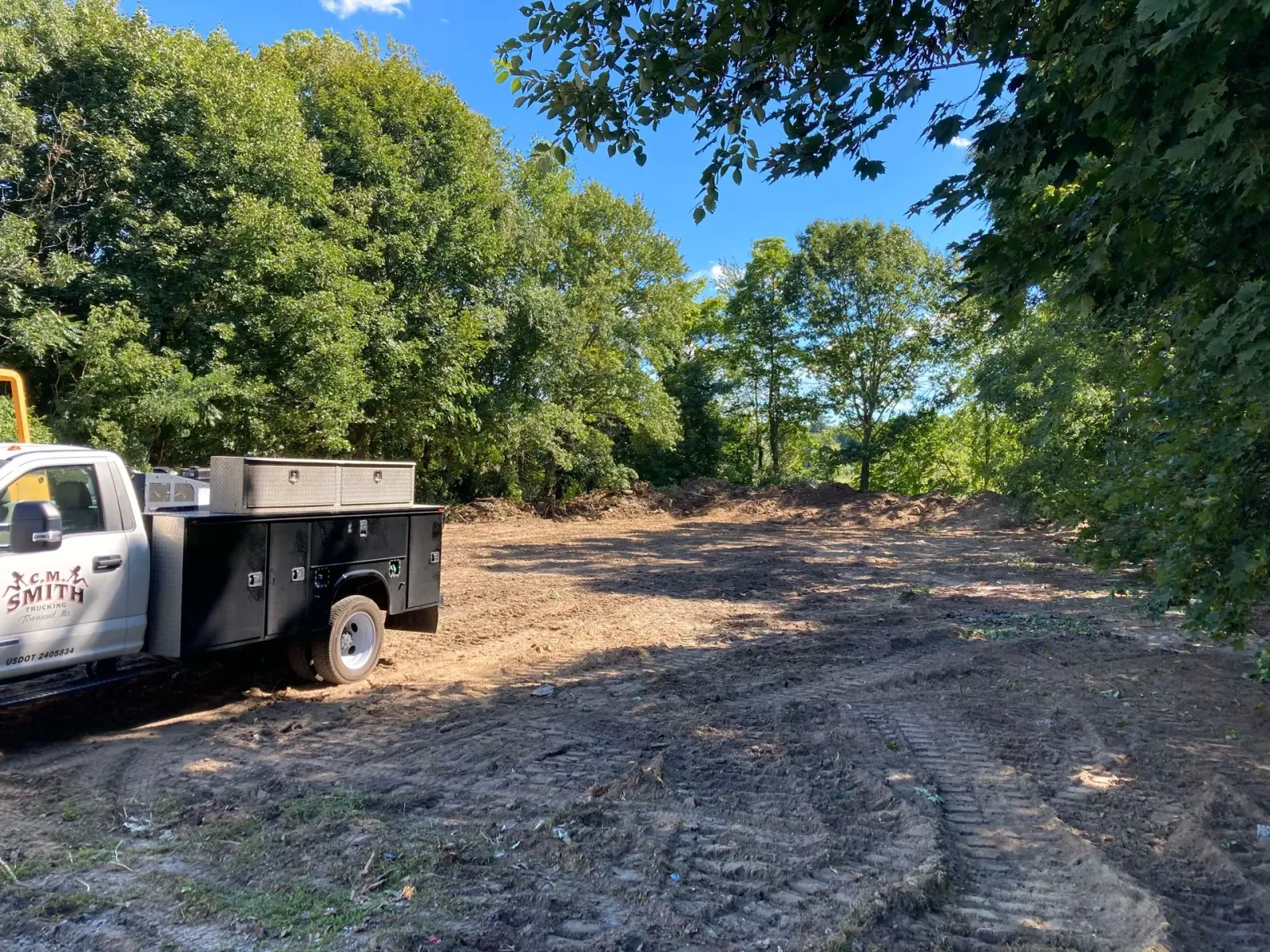 A white truck is parked in a dirt field surrounded by trees.