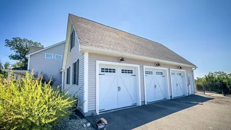 A large garage with three white garage doors is sitting next to a house.