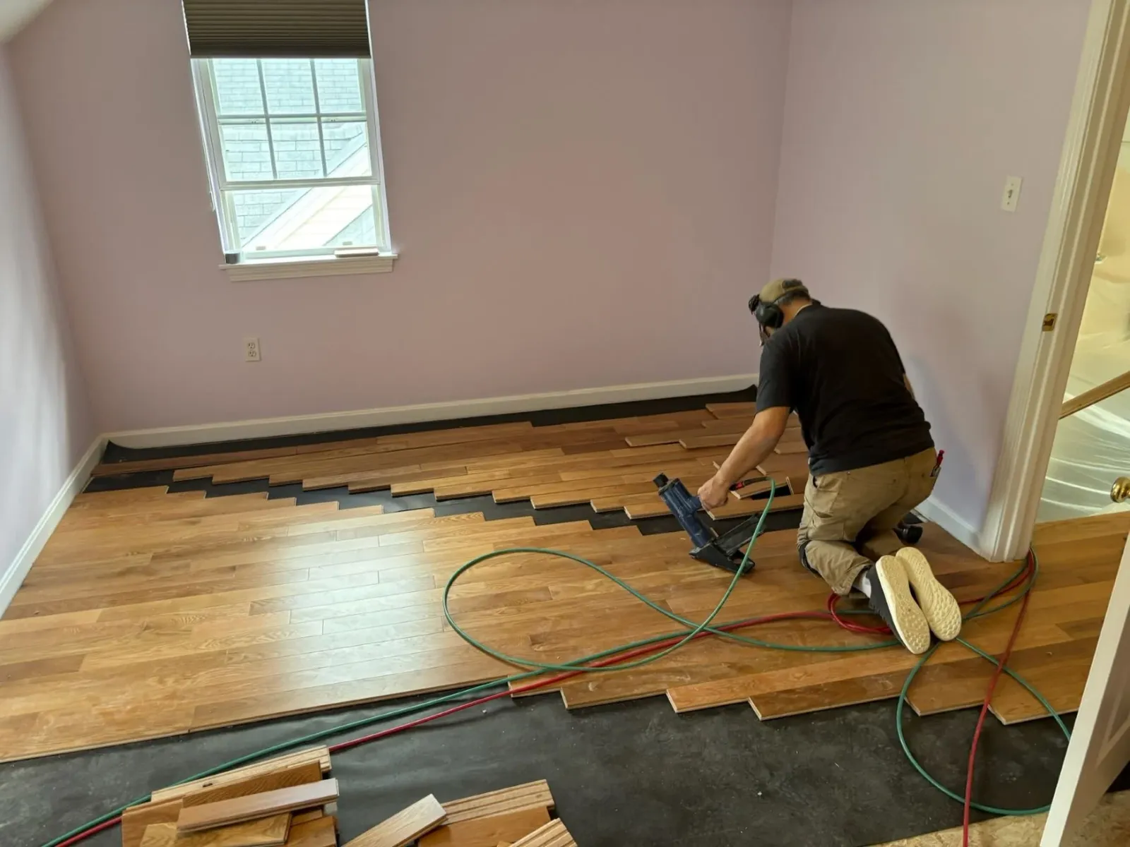 Eric from Finish First Floors laying down and installing the hardwood flooring planks for a new install in a pink bedroom