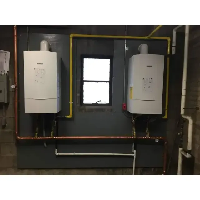 Two white boilers are hanging on a wall next to a window.
