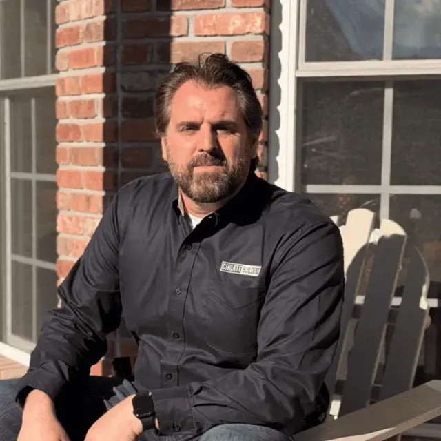Man in black shirt with Choate Builders logo sitting outdoors.