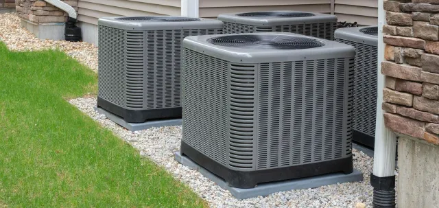 Three air conditioners are sitting outside of a house.