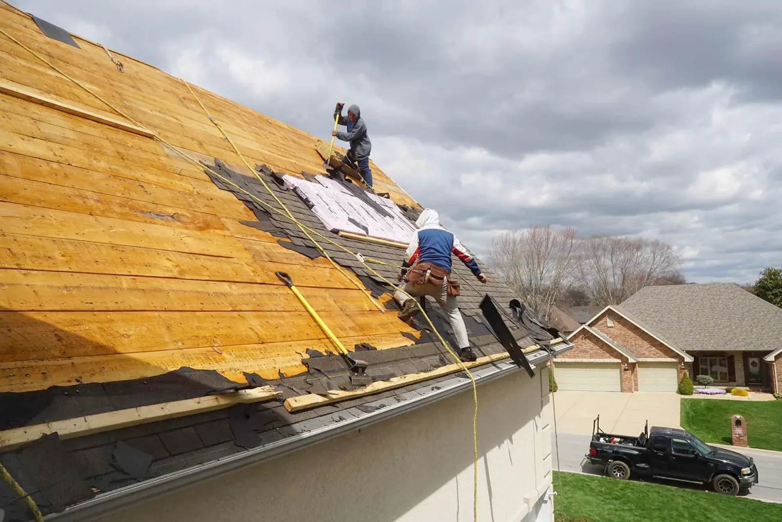 Two roofers replacing shingles on a residential roof, sunny day.