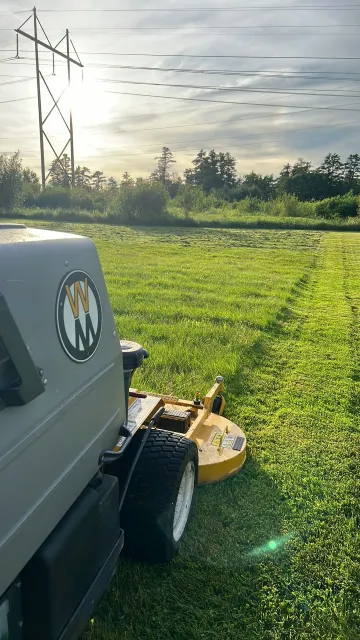 Lawnmower cutting grass in field near power lines. Sunny day.