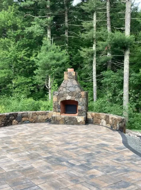 Outdoor stone fireplace with a paved patio, surrounded by trees.