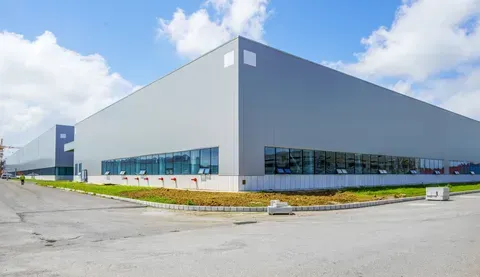 Large gray industrial warehouse with blue windows under a partly cloudy sky