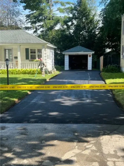 Freshly paved asphalt driveway with yellow caution tape, leading to a garage.