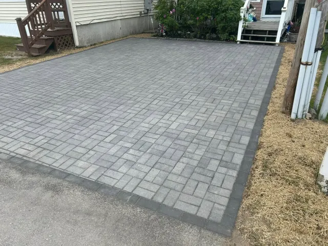 A brick driveway in front of a house with a white fence.