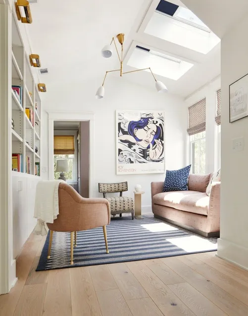 Bright modern living room with skylight, pink sofa, striped rug, and abstract wall art