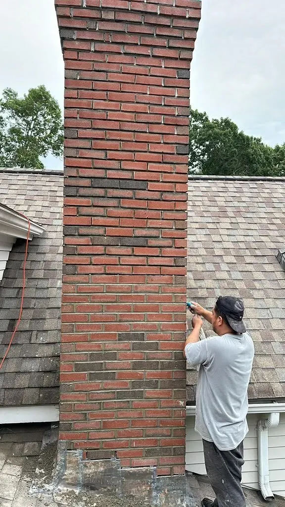 Worker repairing a red brick chimney on a shingled roof outdoors