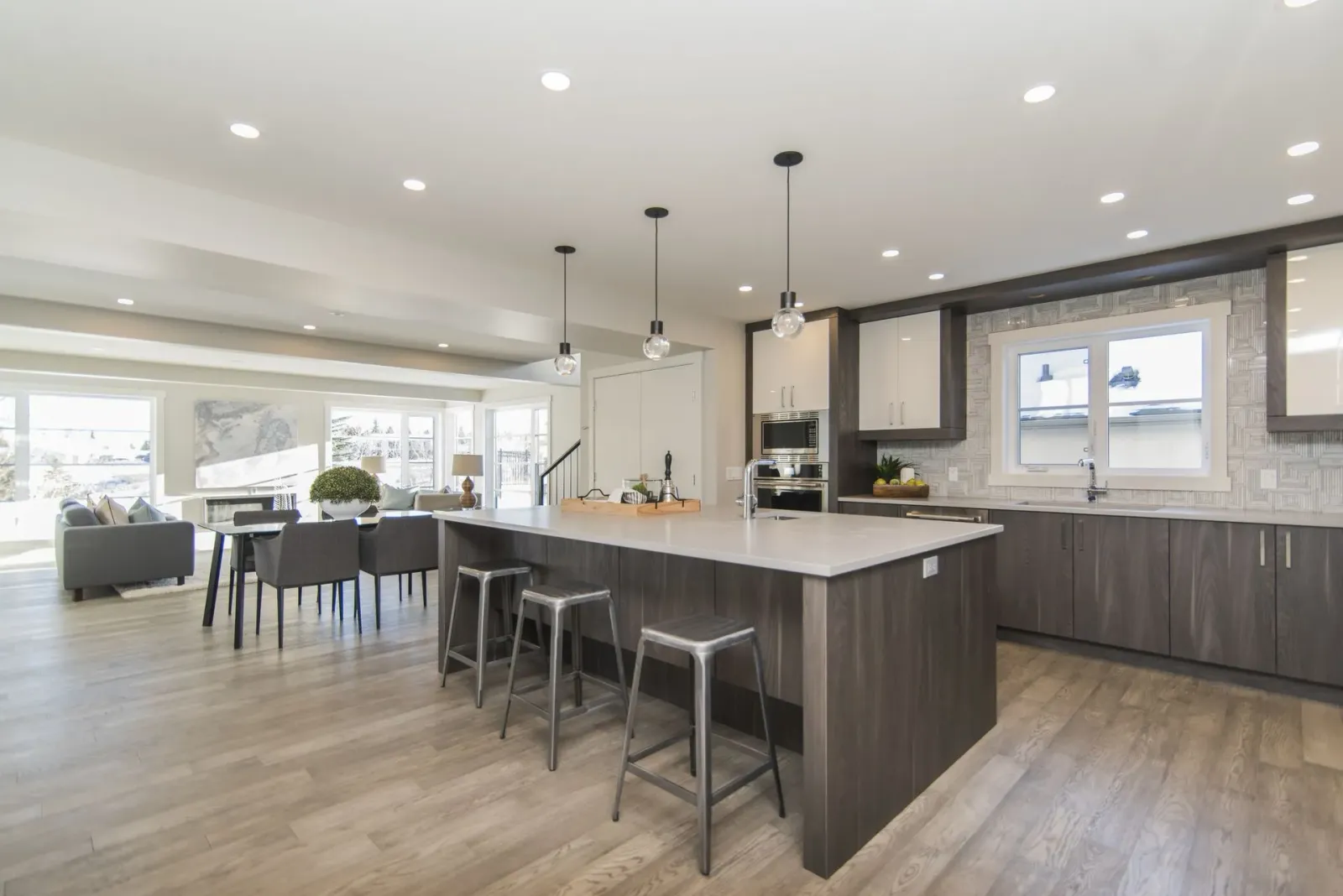 Modern open-plan kitchen with large island, bar stools, gray cabinets, and bright dining area.