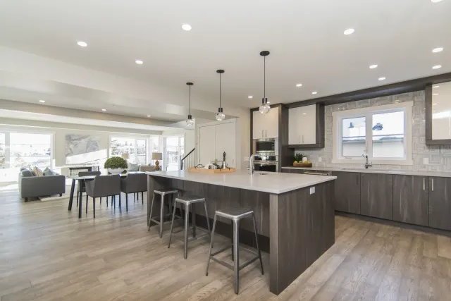Modern open-plan kitchen with large island, bar stools, gray cabinets, and bright dining area.