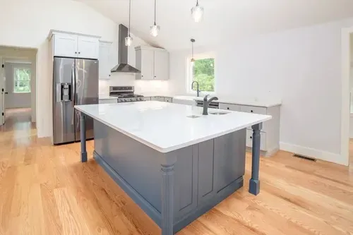 Bright modern kitchen with gray island, white countertops, stainless fridge, and hardwood floors