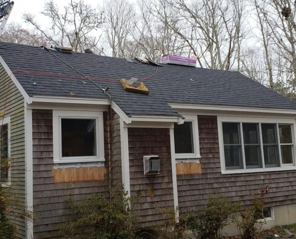 House with gray roof under construction, surrounded by trees, weathered cedar shingles.