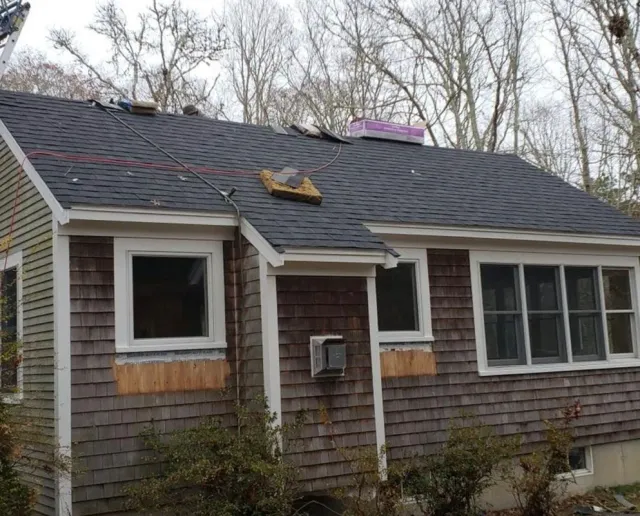 House with gray roof under construction, surrounded by trees, weathered cedar shingles.
