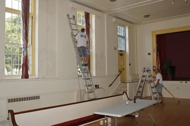 A man on a ladder painting a wall in a room