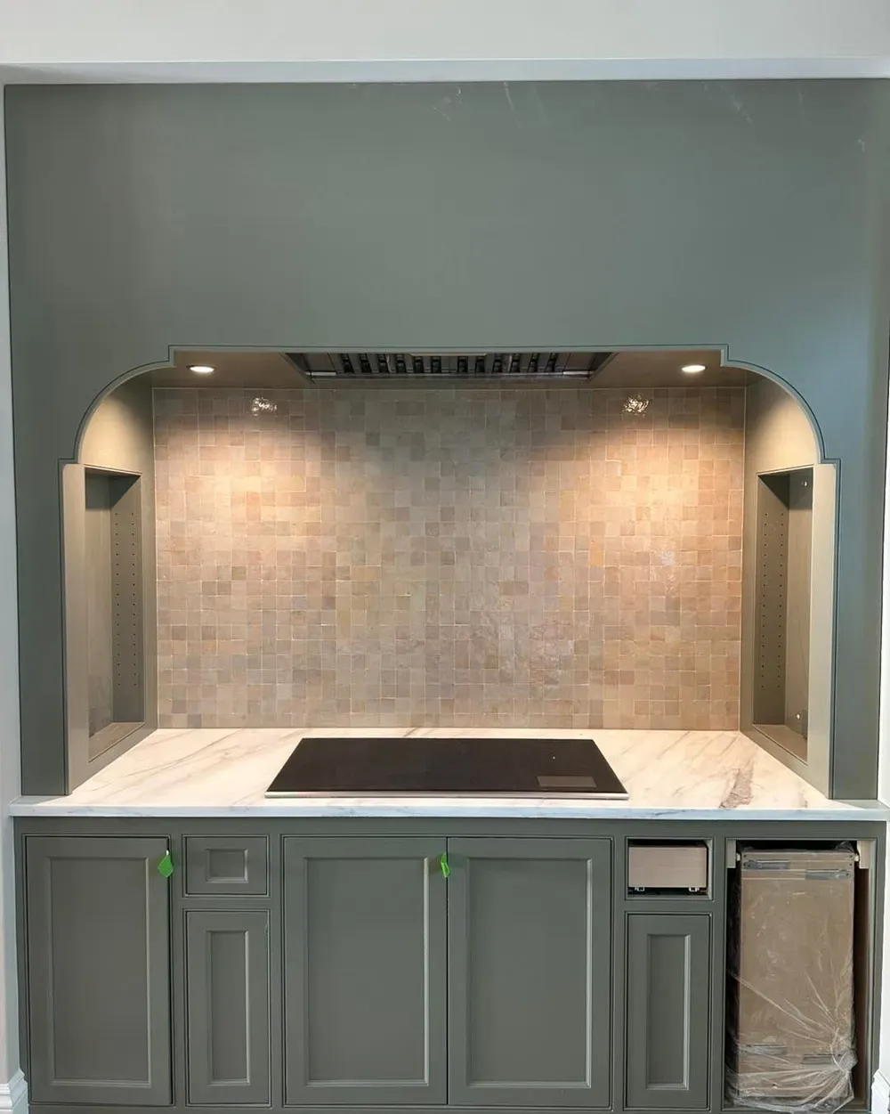 Modern kitchen cooktop alcove with gray cabinets, tiled backsplash, and range hood lighting