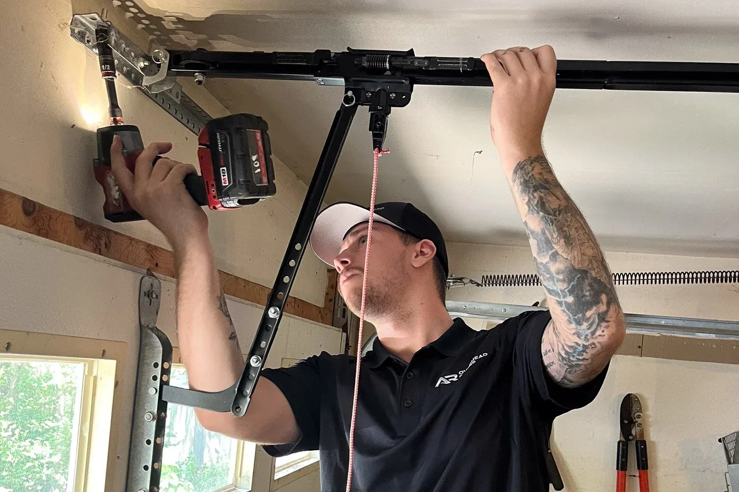 A technician repairing a garage door opener with a power drill in a garage setting.