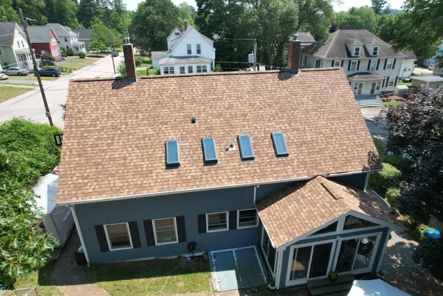 Aerial view of a house with a shingled roof and four skylights in a residential neighborhood.