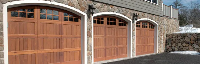 Three arched wood garage doors with top windows set in a stone exterior wall.