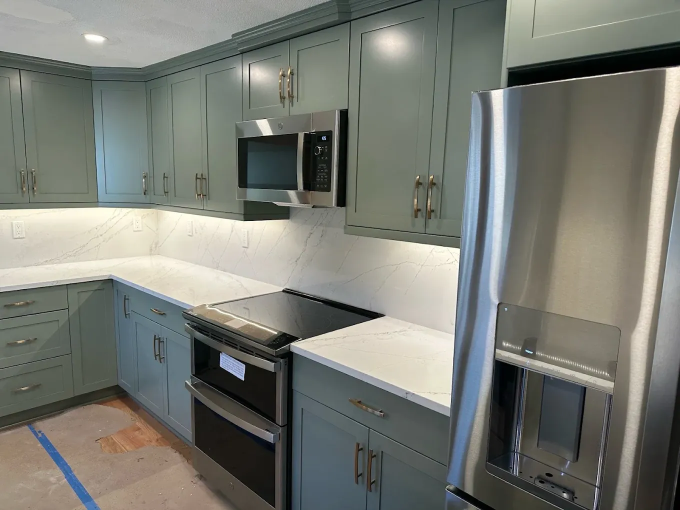 Under-cabinet LED lighting washing a marble backsplash in a kitchen with green cabinets
