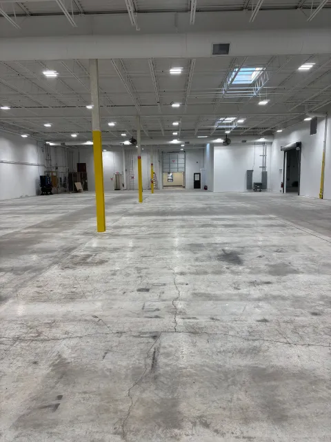 Empty warehouse interior with concrete floor, white walls, and yellow support beams.