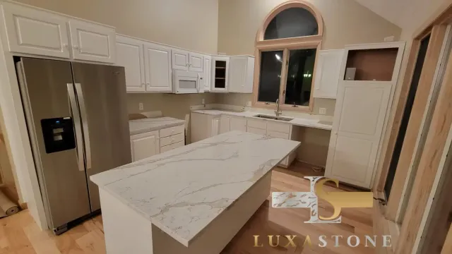 Kitchen with white cabinets, island, and light countertops; stainless steel refrigerator.