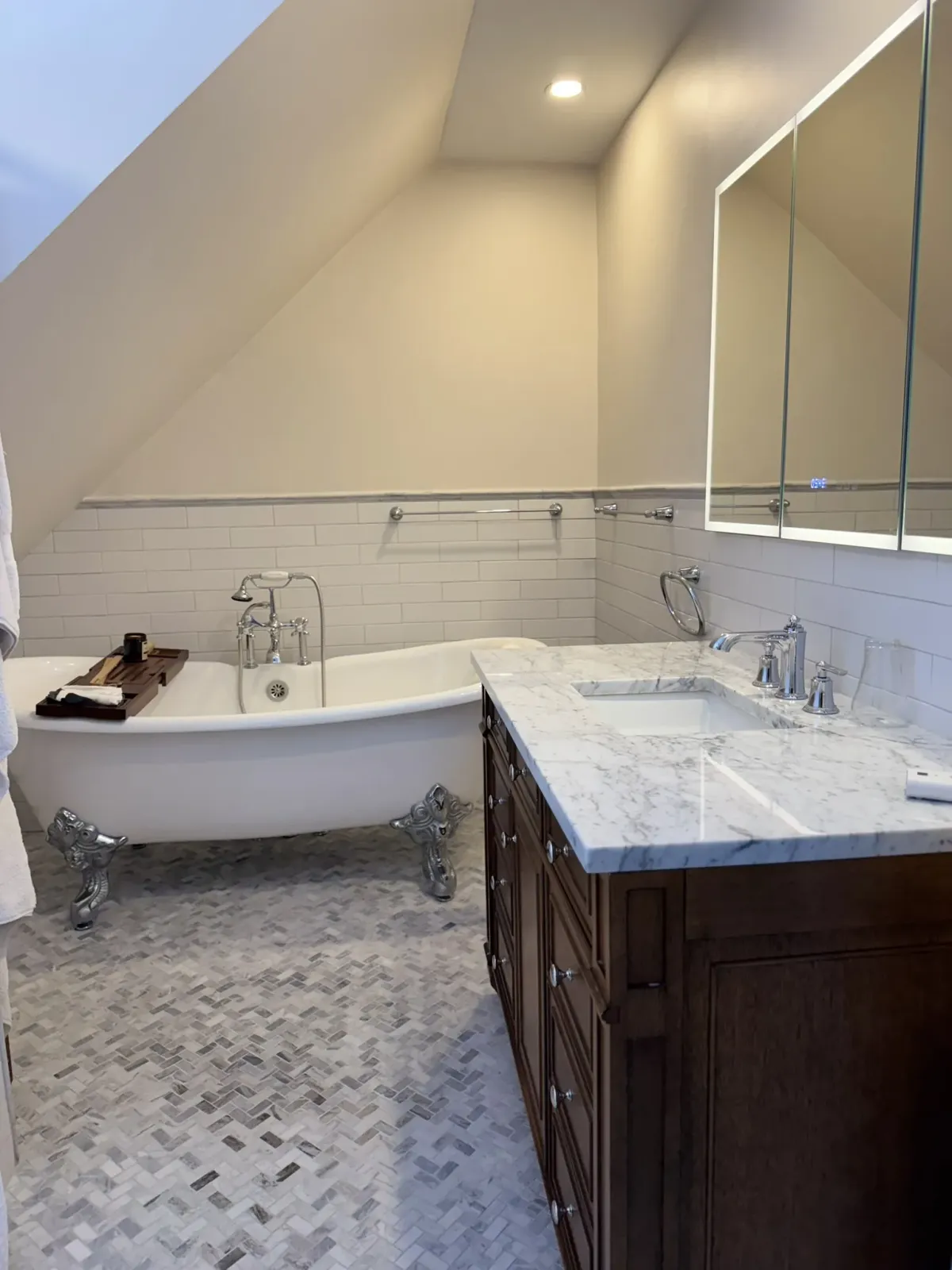 Bathroom with a dark wood vanity, marble top and a freestanding tub on herringbone tile