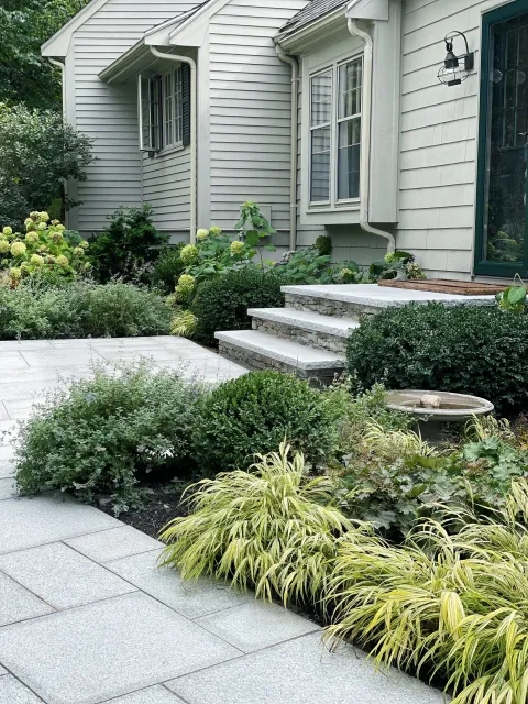 A front yard garden that includes new stone steps and landings, a granite pathway and beautiful garden design that offers superior curb appeal at this Andover landscape.